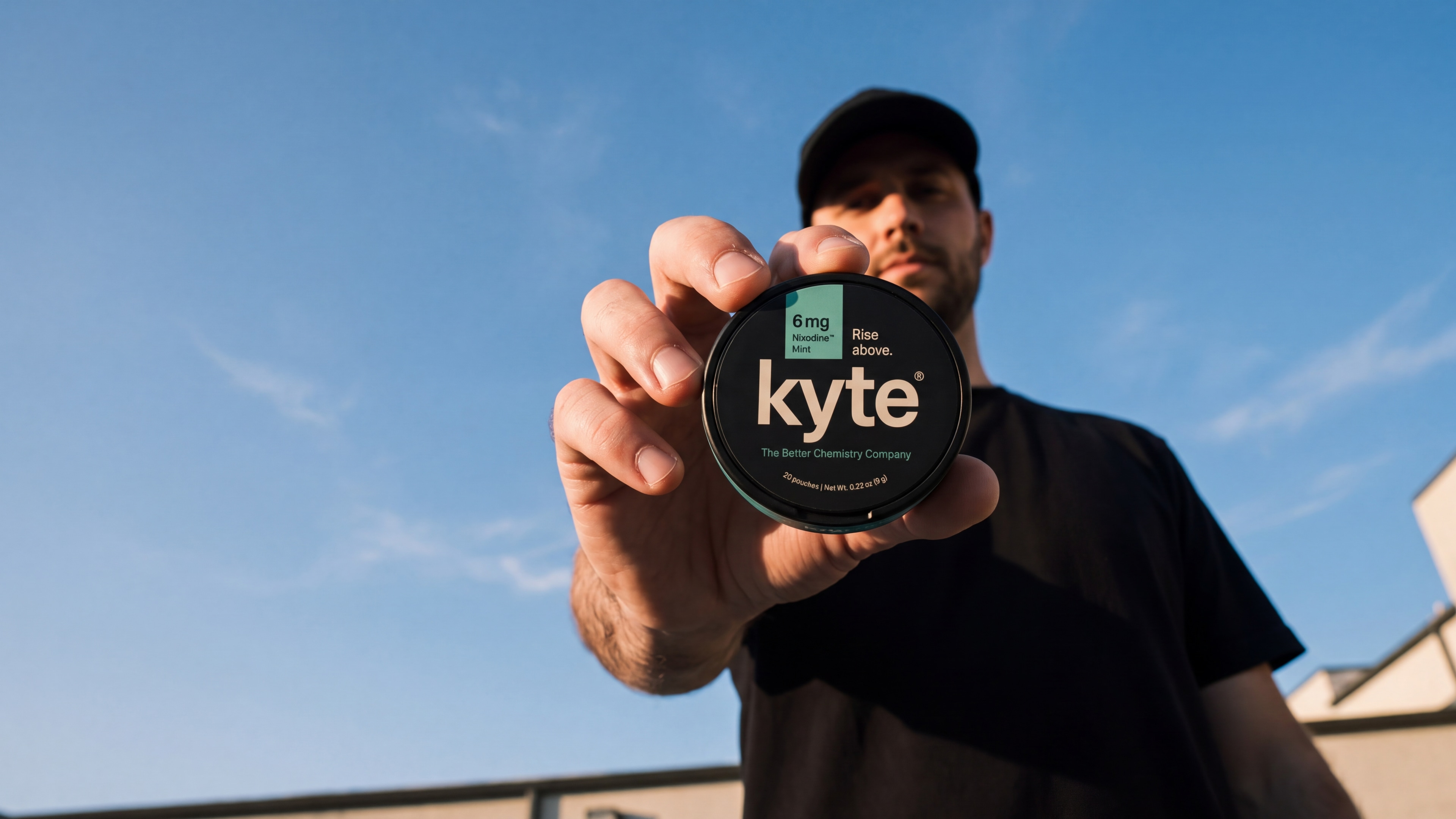 Man holding a Kyte Mint tin against open sky